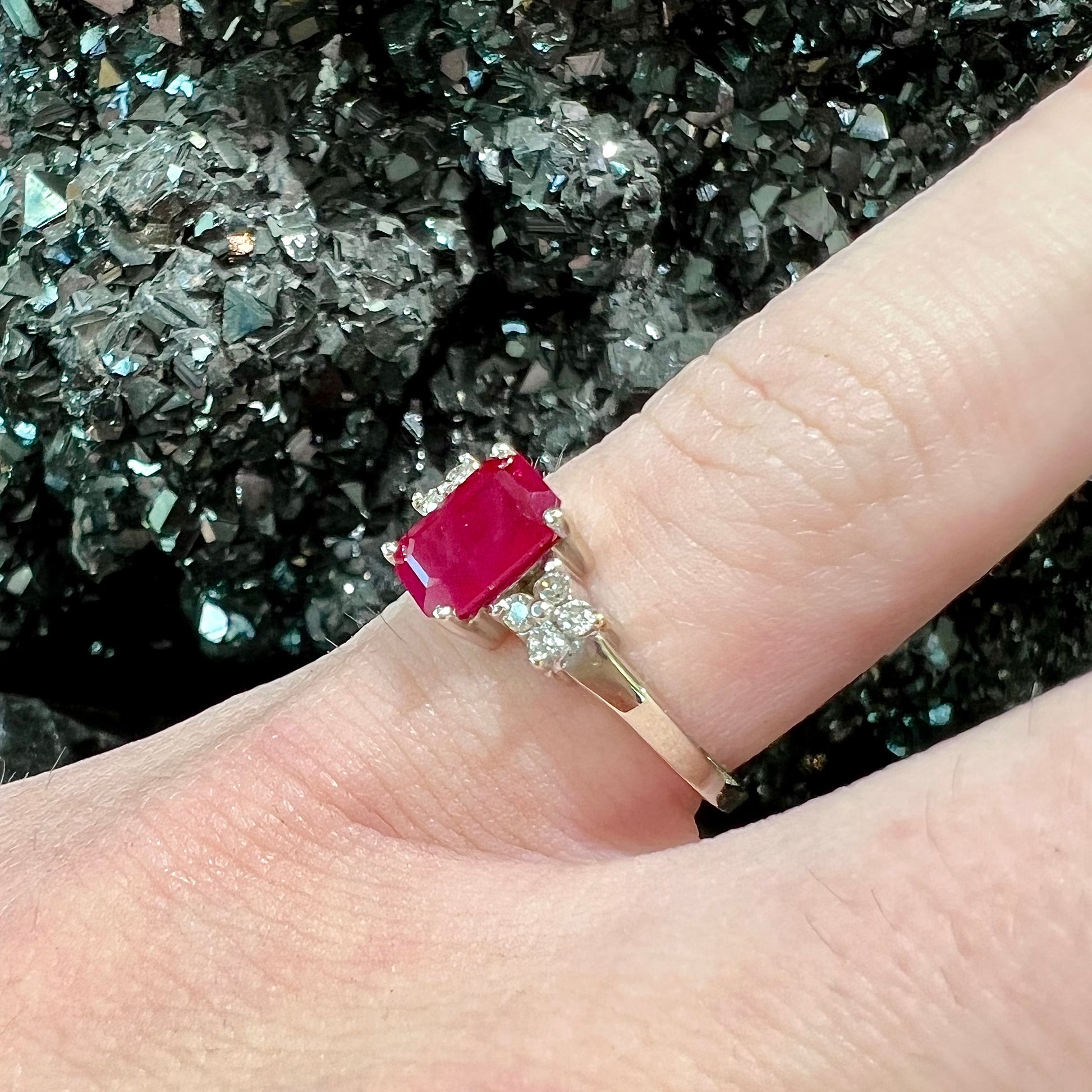 A white gold ring with an emerald cut red synthetic ruby set between four round cut diamonds on each side.
