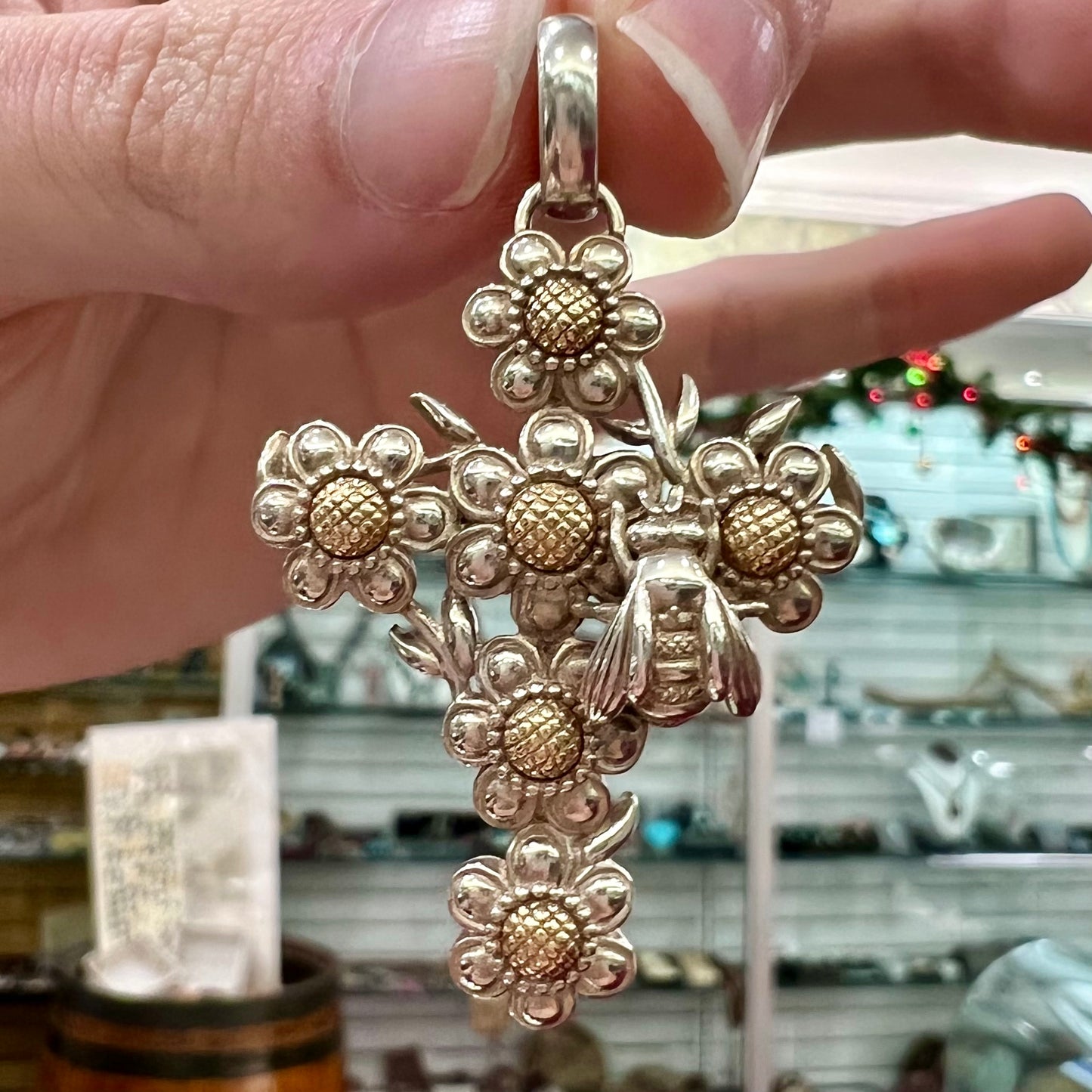 A cross pendant with floral decoration.  The cross is made of six  flowers with sterling silver petals and yellow gold nectar.  A silver bee is on one of the pendants.  The bail opens and closes.