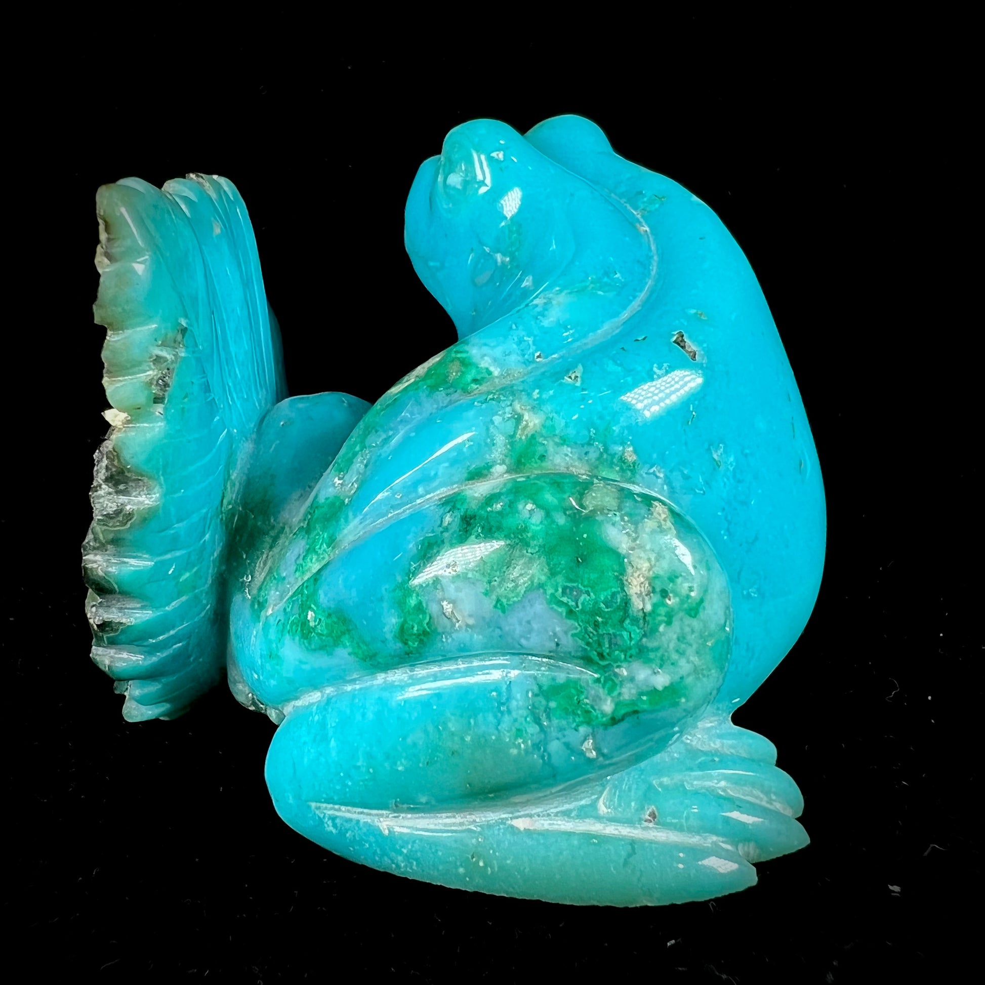 A stone frog peeking from behind a leaf carved from gem silica grade chrysocolla by artist, Ron Stevens.