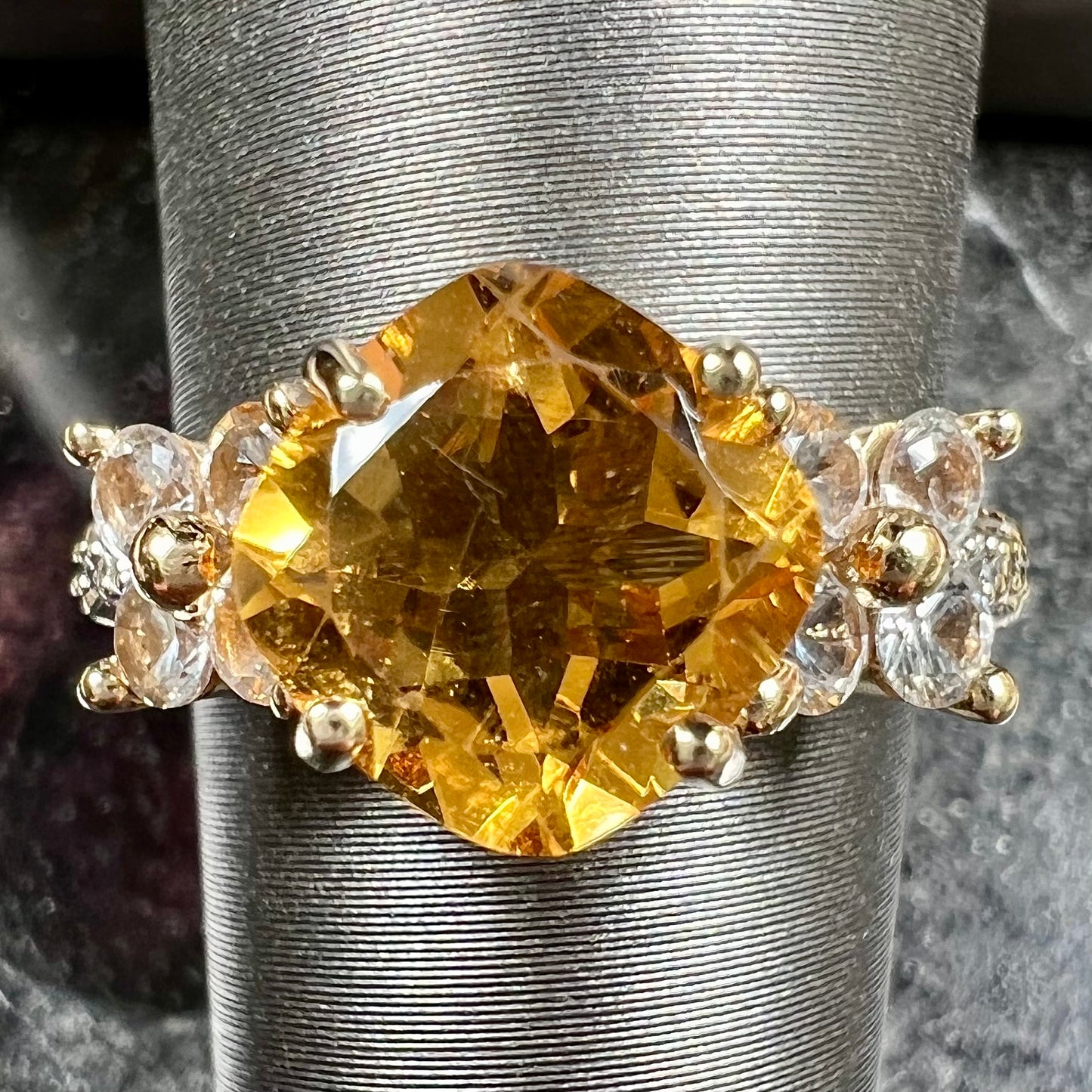 A cushion cut citrine set in a yellow gold ring with four round white sapphires and two diamonds on each side.