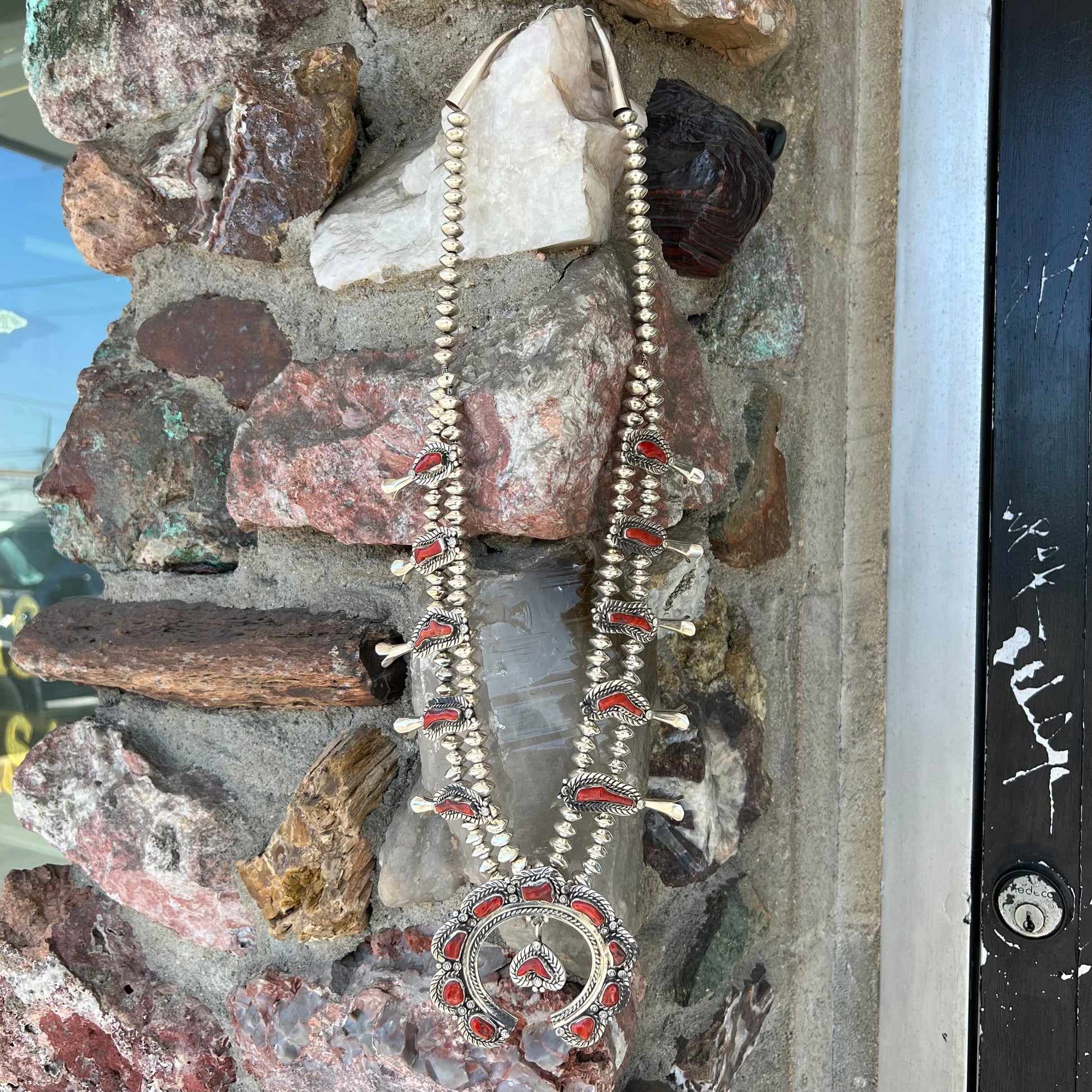 A Navajo style squash blossom necklace set with red coral branches, handmade by artist Delbert Chatter.