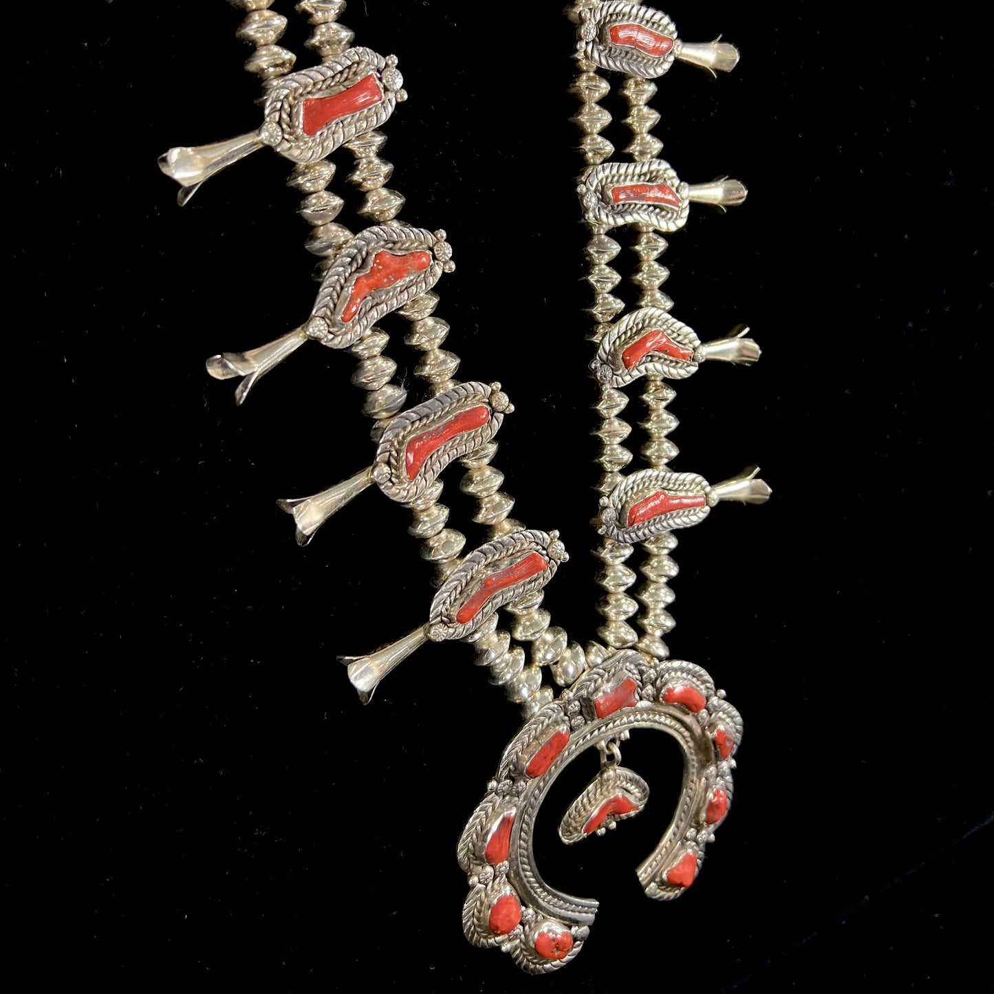 A Navajo style squash blossom necklace set with red coral branches, handmade by artist Delbert Chatter.