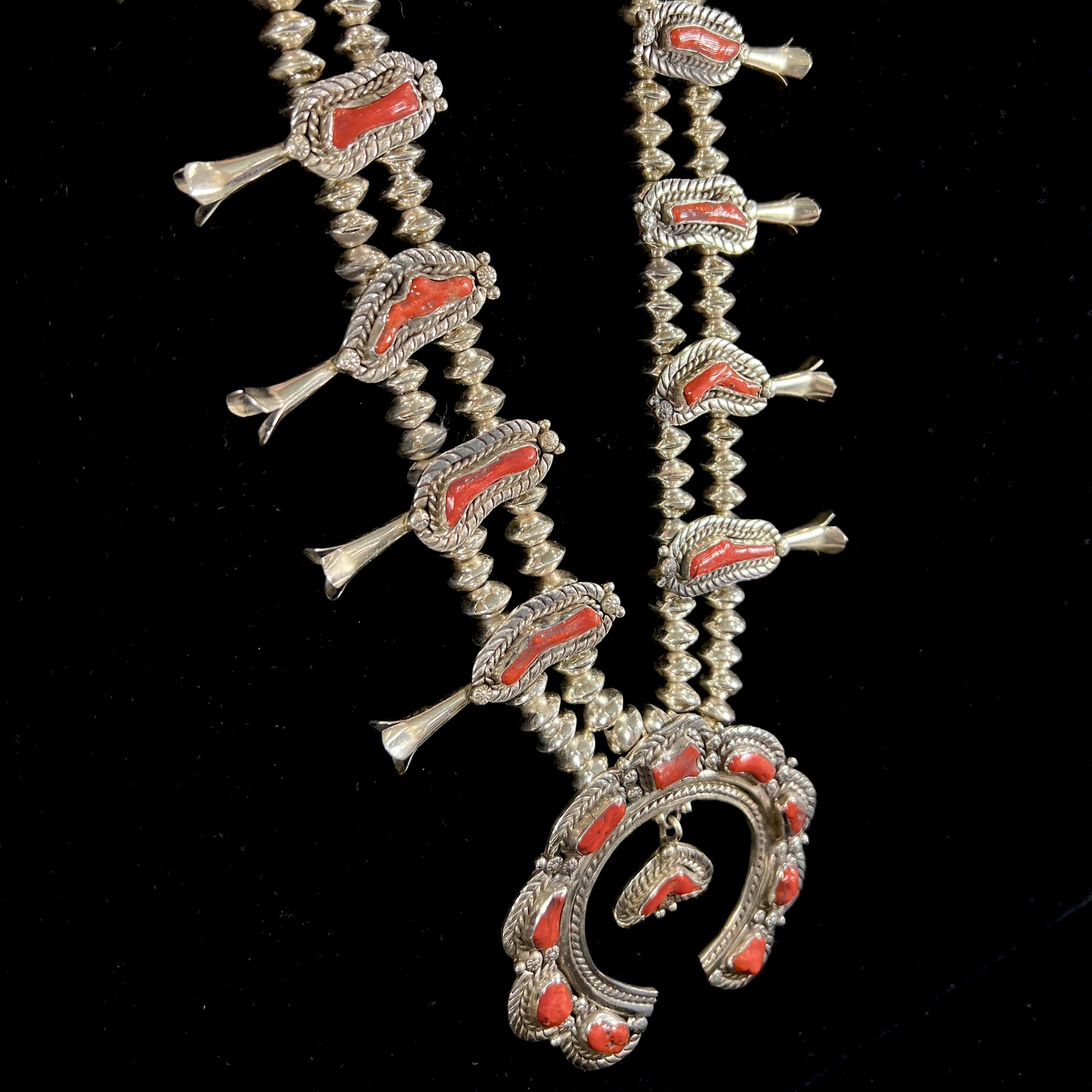 A Navajo style squash blossom necklace set with red coral branches, handmade by artist Delbert Chatter.