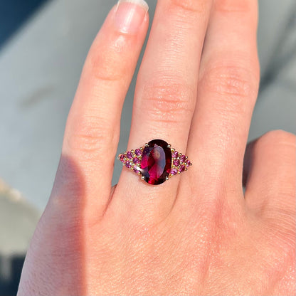 A ring with a crimson reddish purple stone set with clusters of round purple garnets on each side.
