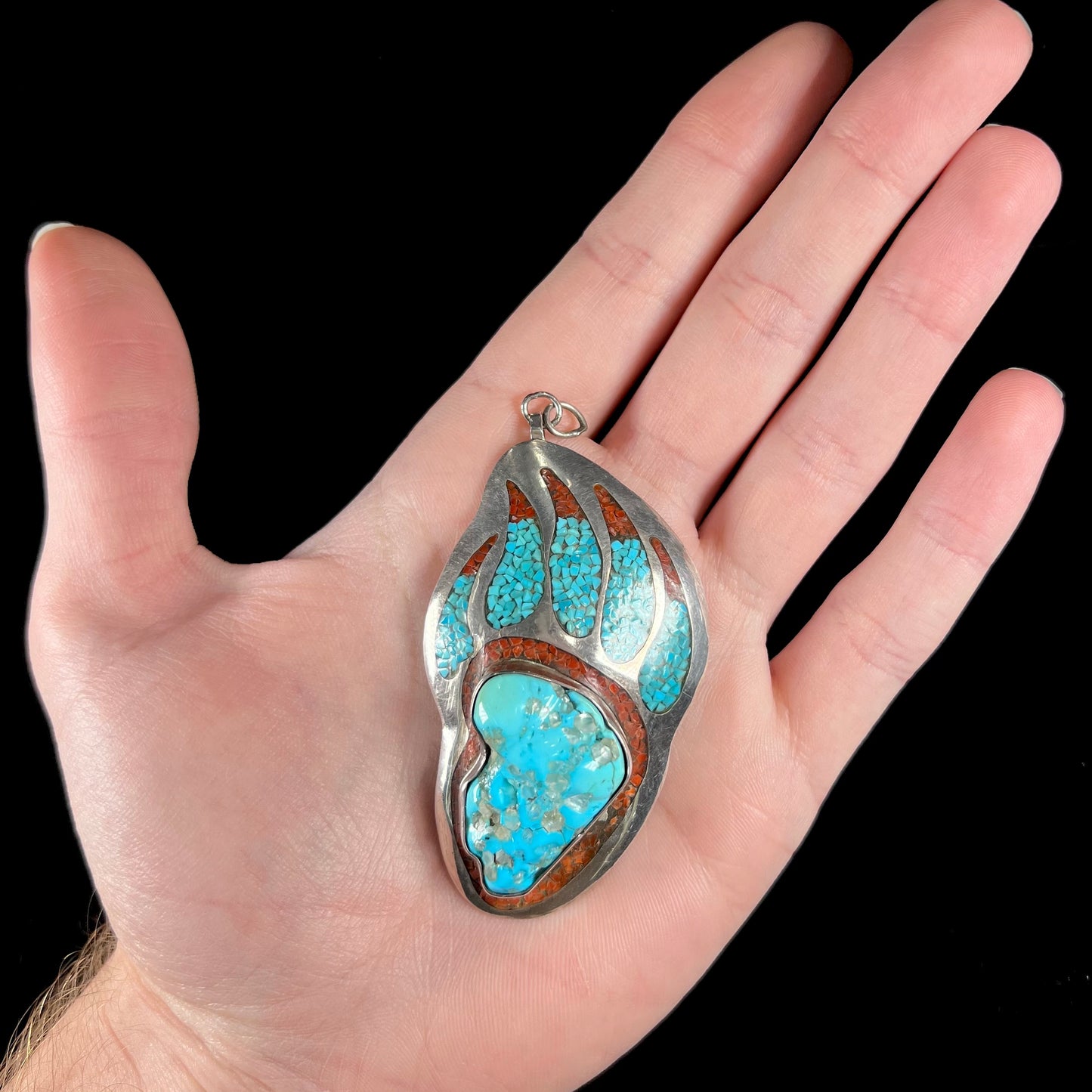 A sterling silver bear paw pendant set with Sleeping Beauty turquoise, crushed turquoise, and crushed coral.