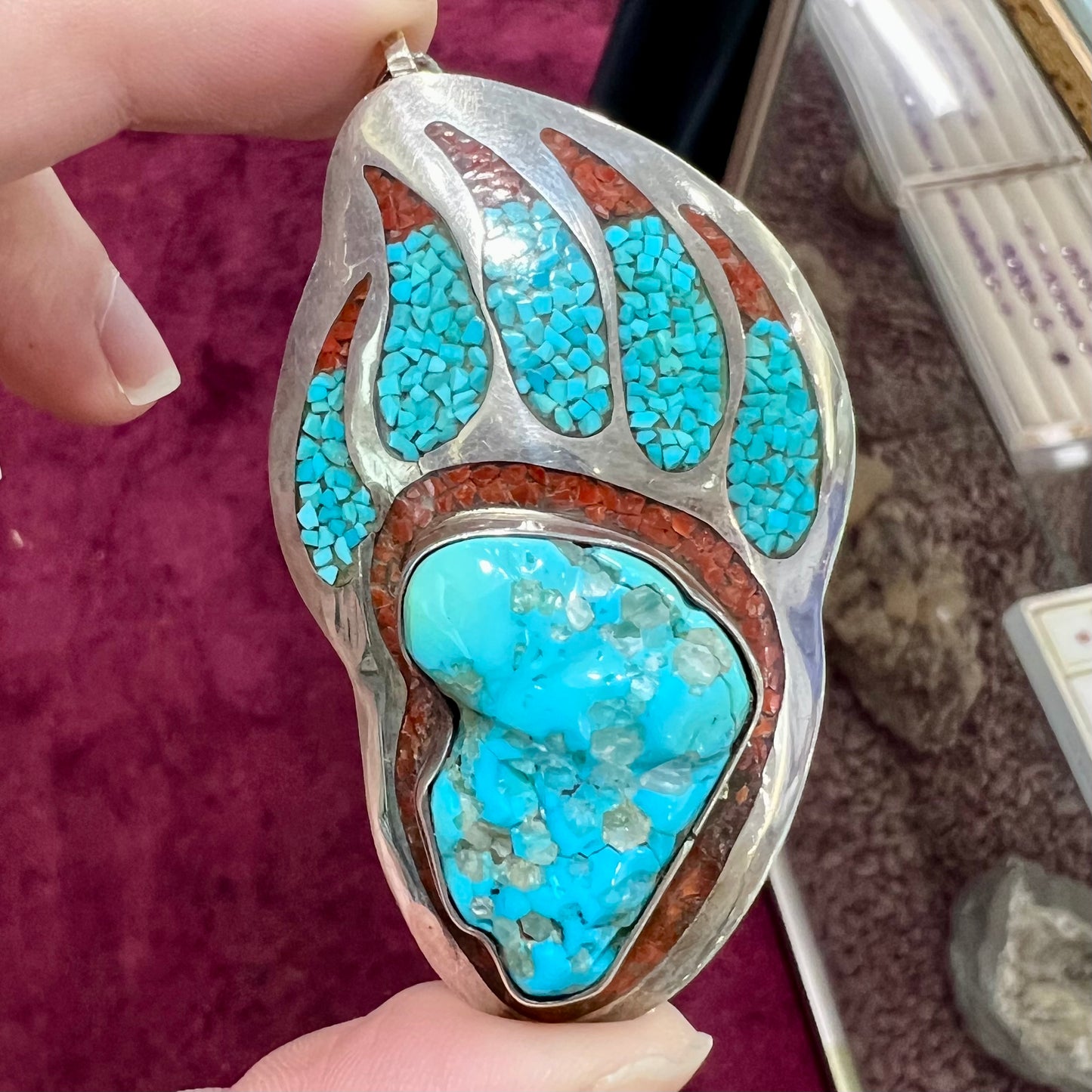 A sterling silver bear paw pendant set with Sleeping Beauty turquoise, crushed turquoise, and crushed coral.