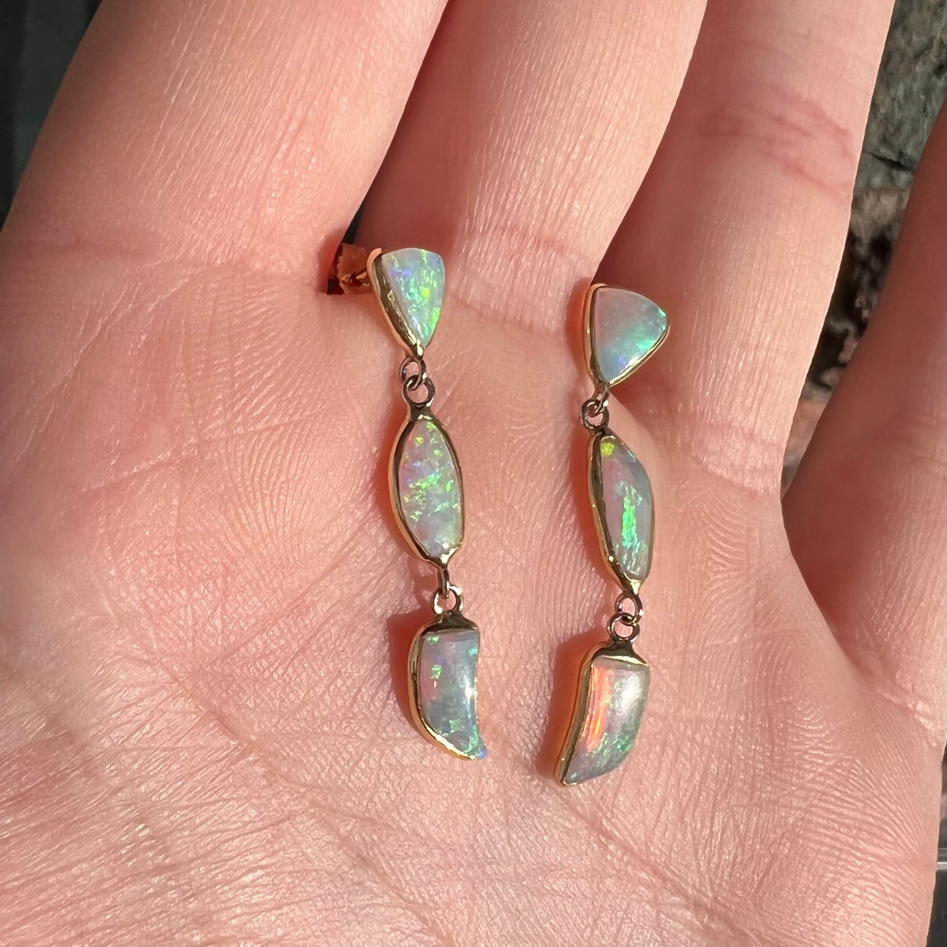 A pair of yellow gold push-back dangle earrings set with three white crystal opals in each.