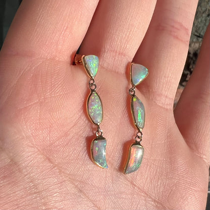 A pair of yellow gold push-back dangle earrings set with three white crystal opals in each.