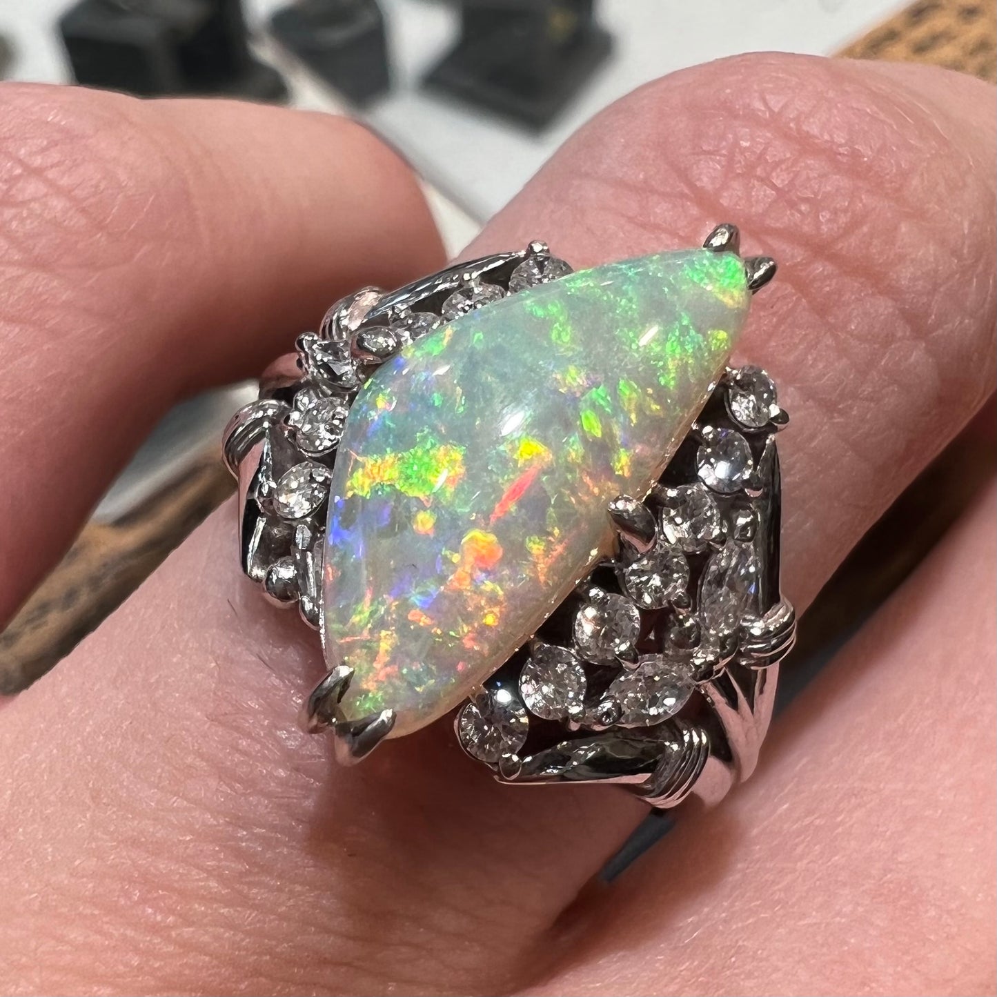 A freeform triangular cabochon cut Lightning Ridge white crystal opal set with diamonds in an ornate platinum split shank setting.