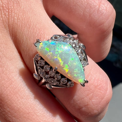 A freeform triangular cabochon cut Lightning Ridge white crystal opal set with diamonds in an ornate platinum split shank setting.