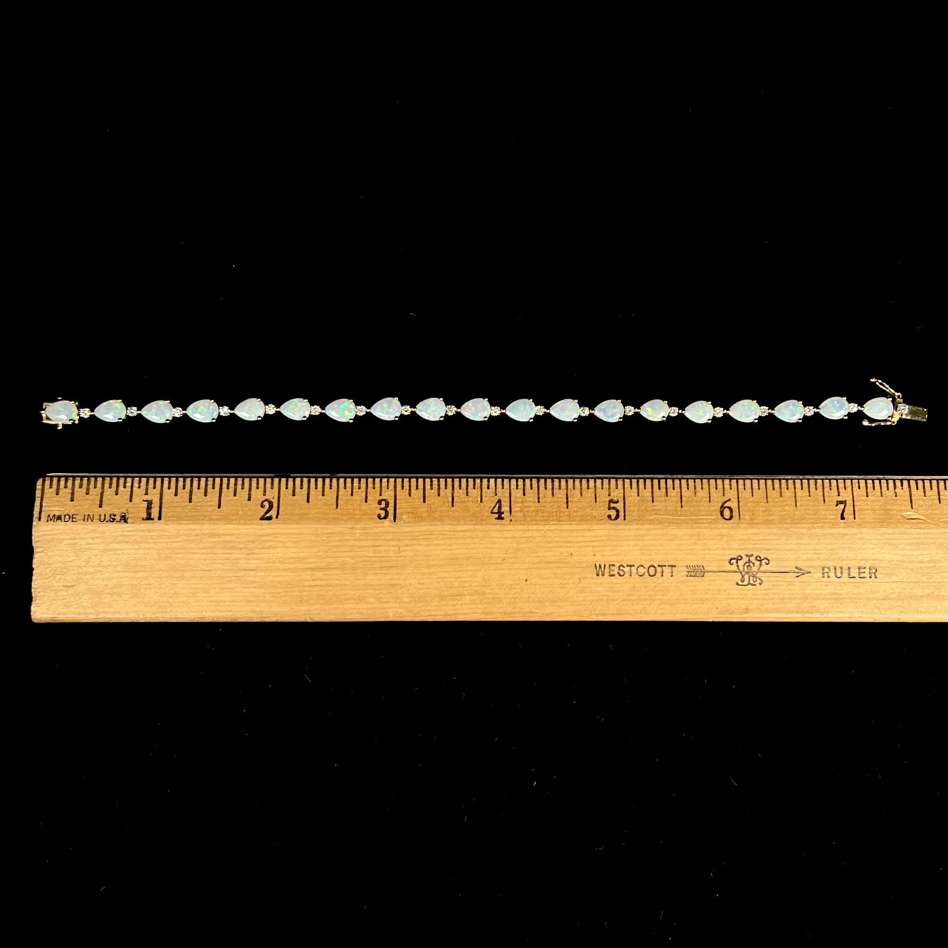 A ladies' gold tennis style bracelet set with pear shaped white crystal opals and diamonds.