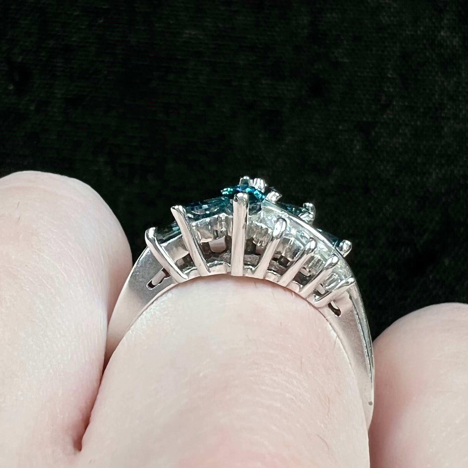 A white gold diamond cluster ring set with blue marquise cut and white round cut diamonds.
