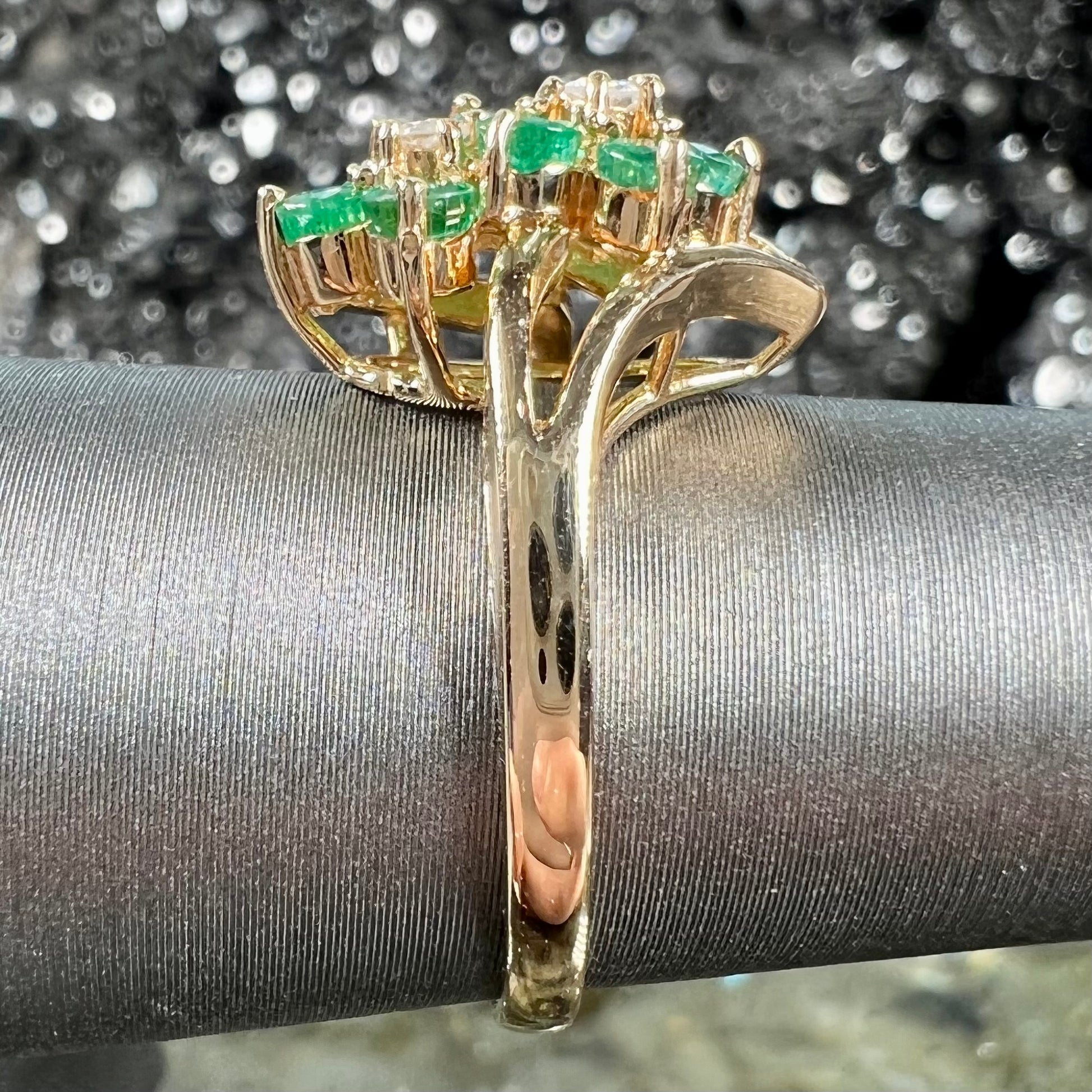 A yellow gold ring set with round cut emerald and diamonds that form the shape of two flowers.