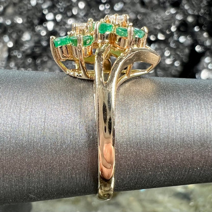 A yellow gold ring set with round cut emerald and diamonds that form the shape of two flowers.