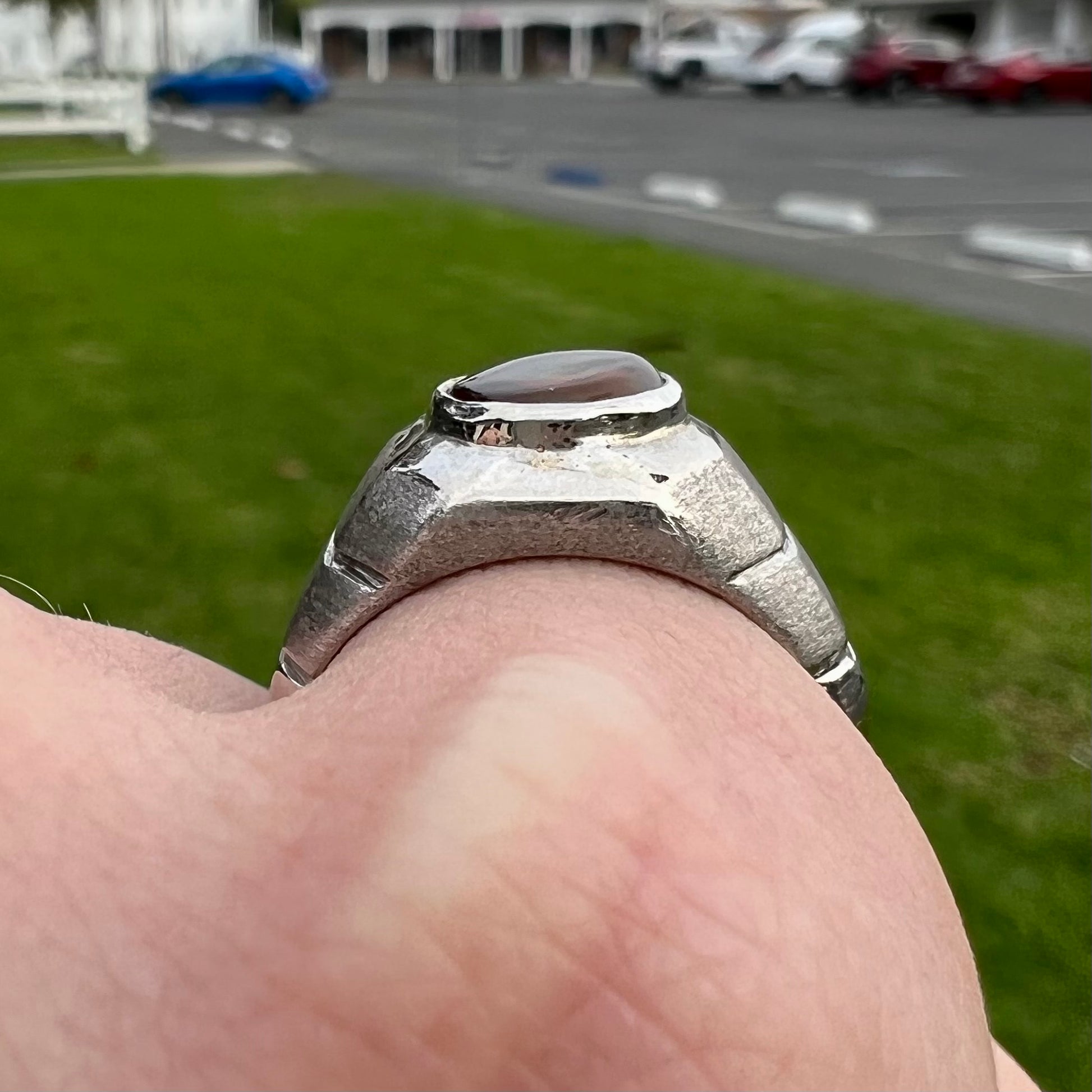 A round cabochon cut red and green fire agate set in a brushed metal white gold men's ring.