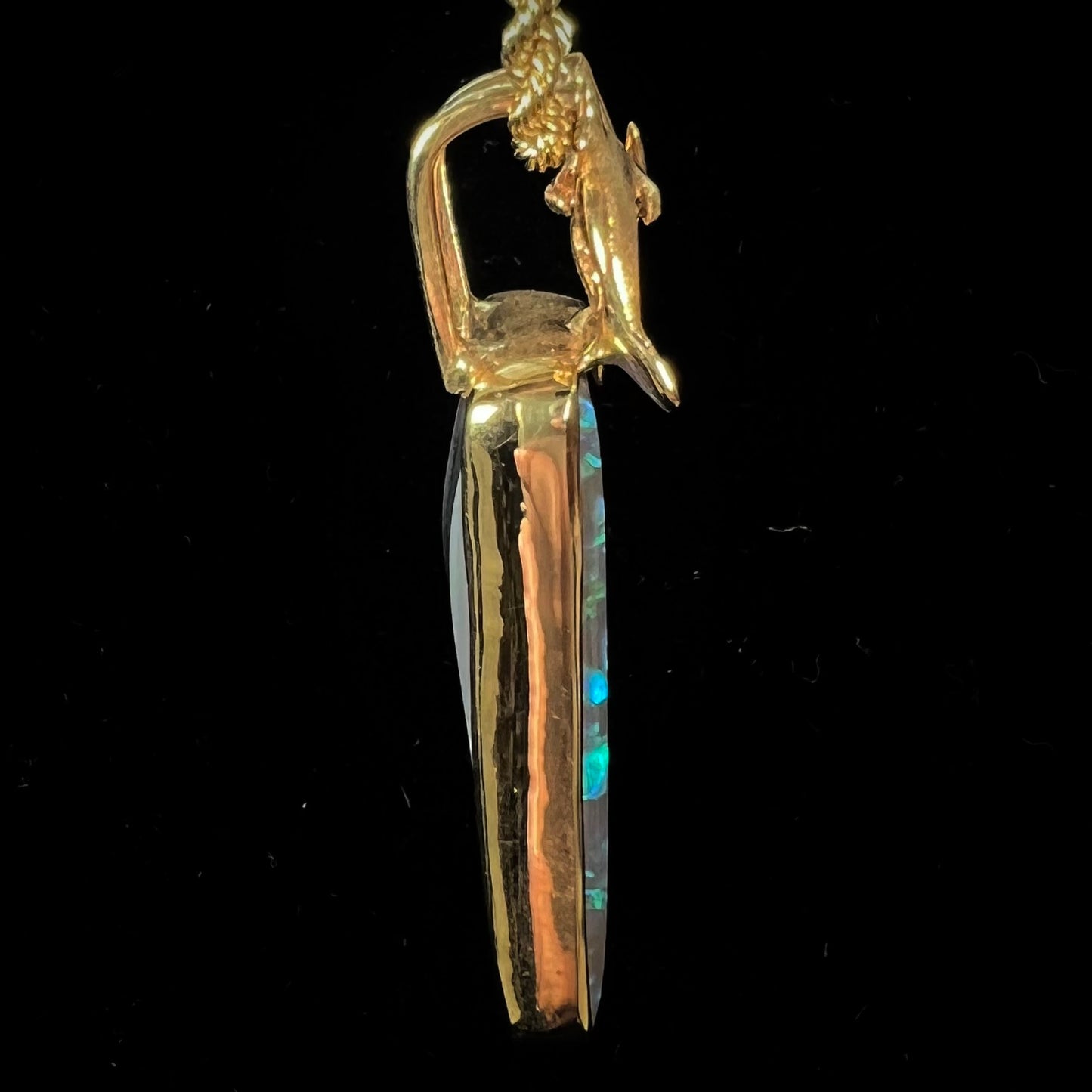 A gold freeform cut black opal bezel pendant cast with two dolphins on top of the opal.