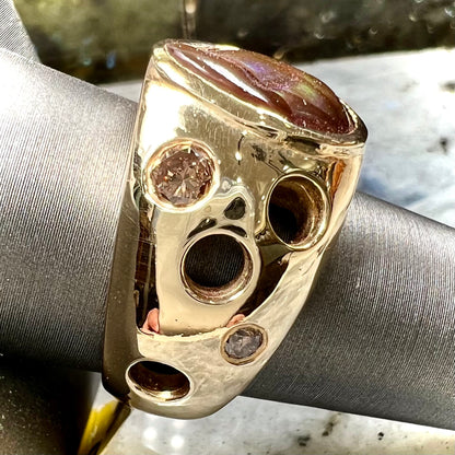 Men's rainbow fire agate ring set in yellow gold with champagne diamonds.  The ring style has holes.