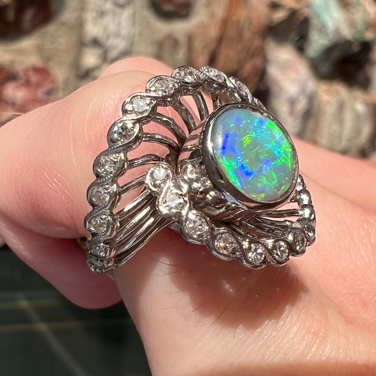 A white gold ring featuring a round cabochon cut black opal set in a swirl of round cut diamonds.