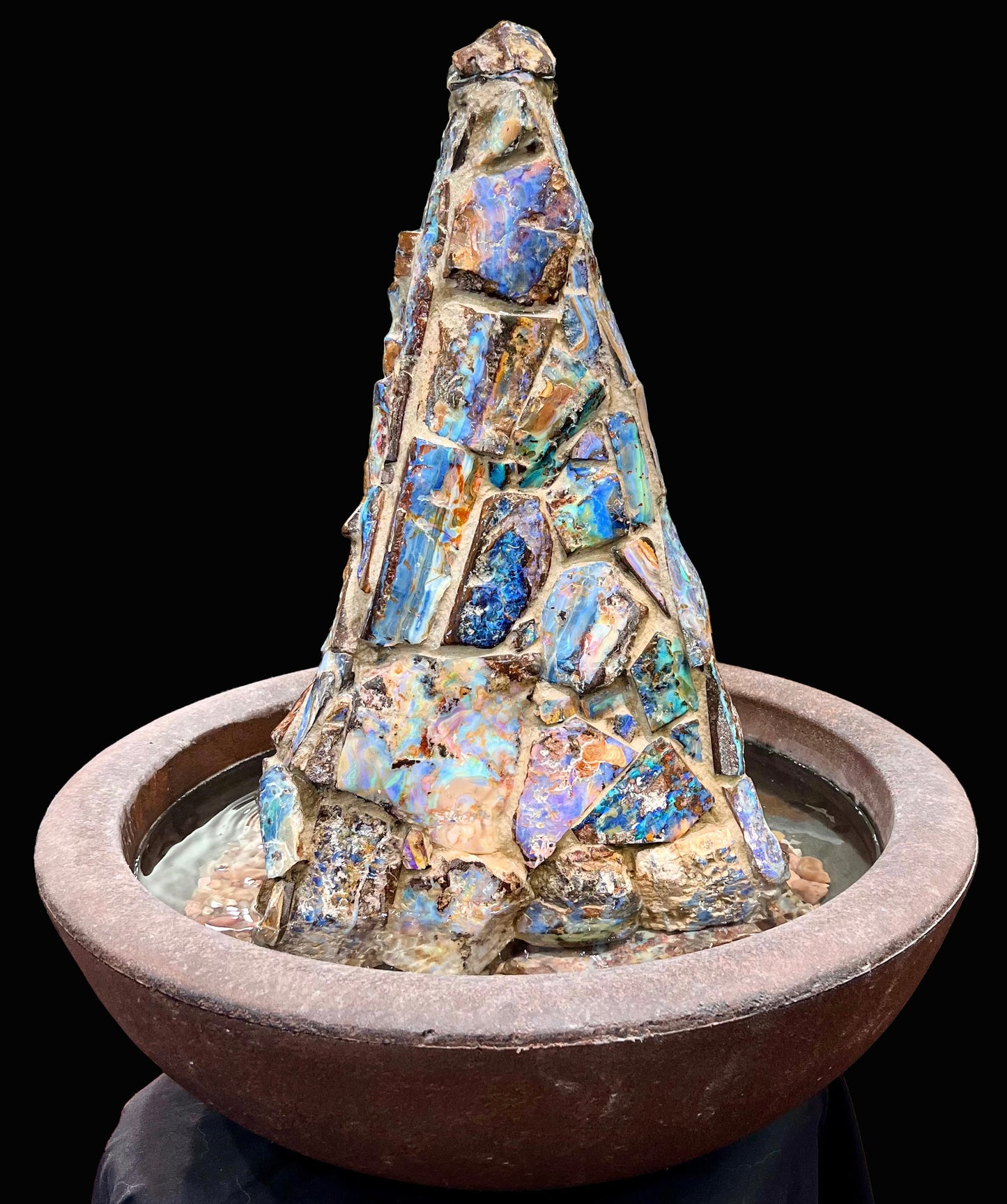 An indoor/outdoor three sided pyramid fountain made from Australian boulder opal, sitting in a bowl of Mexican fire opal.