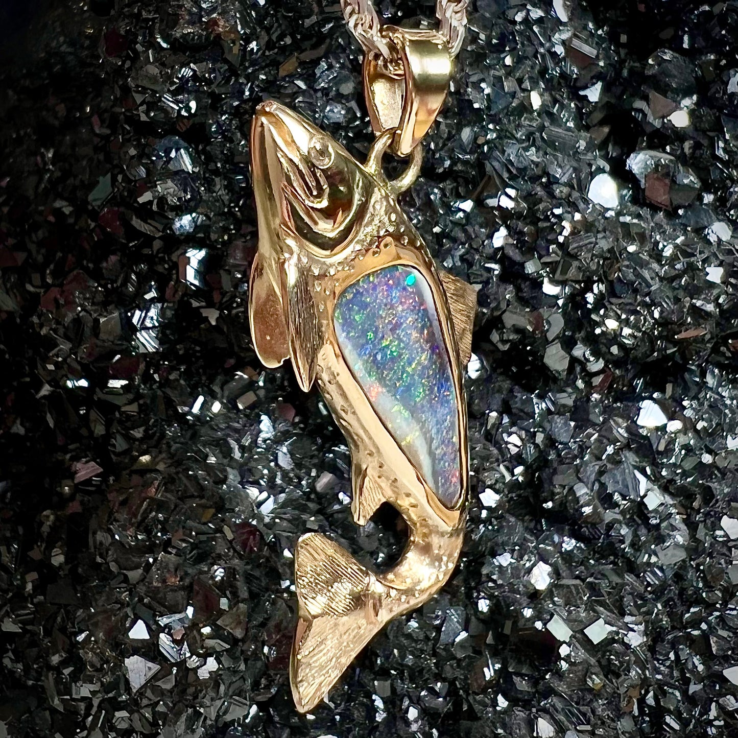 A yellow gold fish pendant detailed to look like a rainbow trout.  The body of the fish is set with a color changing black opal stone.