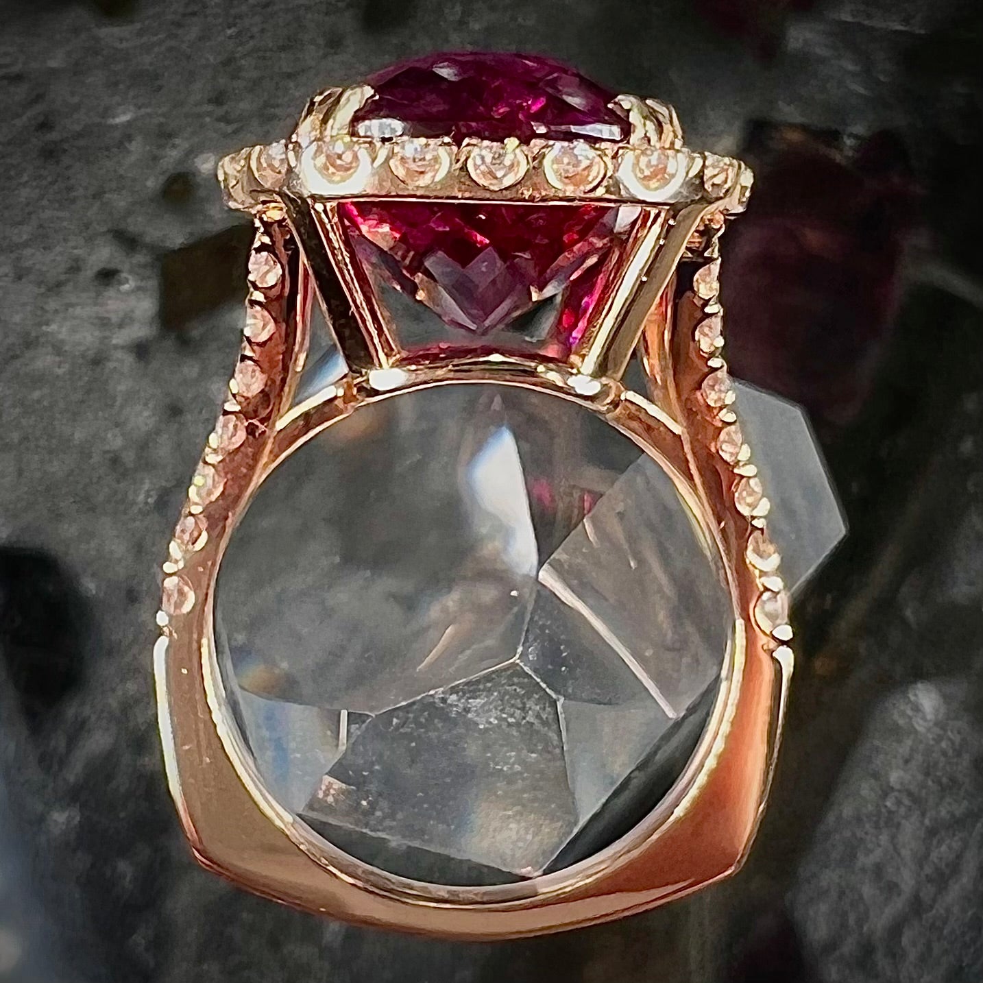 A rose gold, split shank engagement ring set with a cushion cut rubellite tourmaline in a diamond halo.