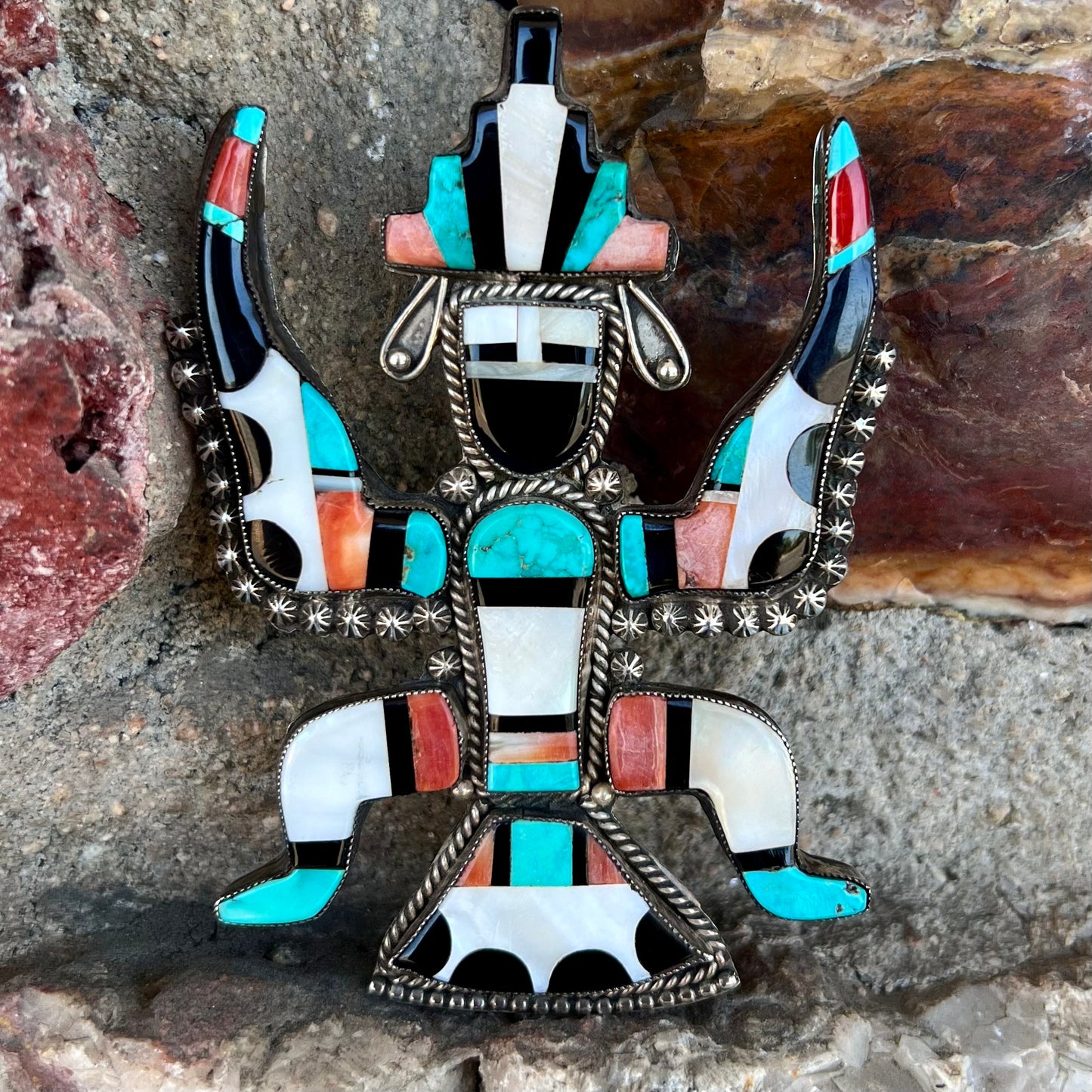 A silver, Zuni Indian dancing eagle necklace/pin.  The piece is inlaid with pieces of onyx, turquoise, coral, and mother of pearl.