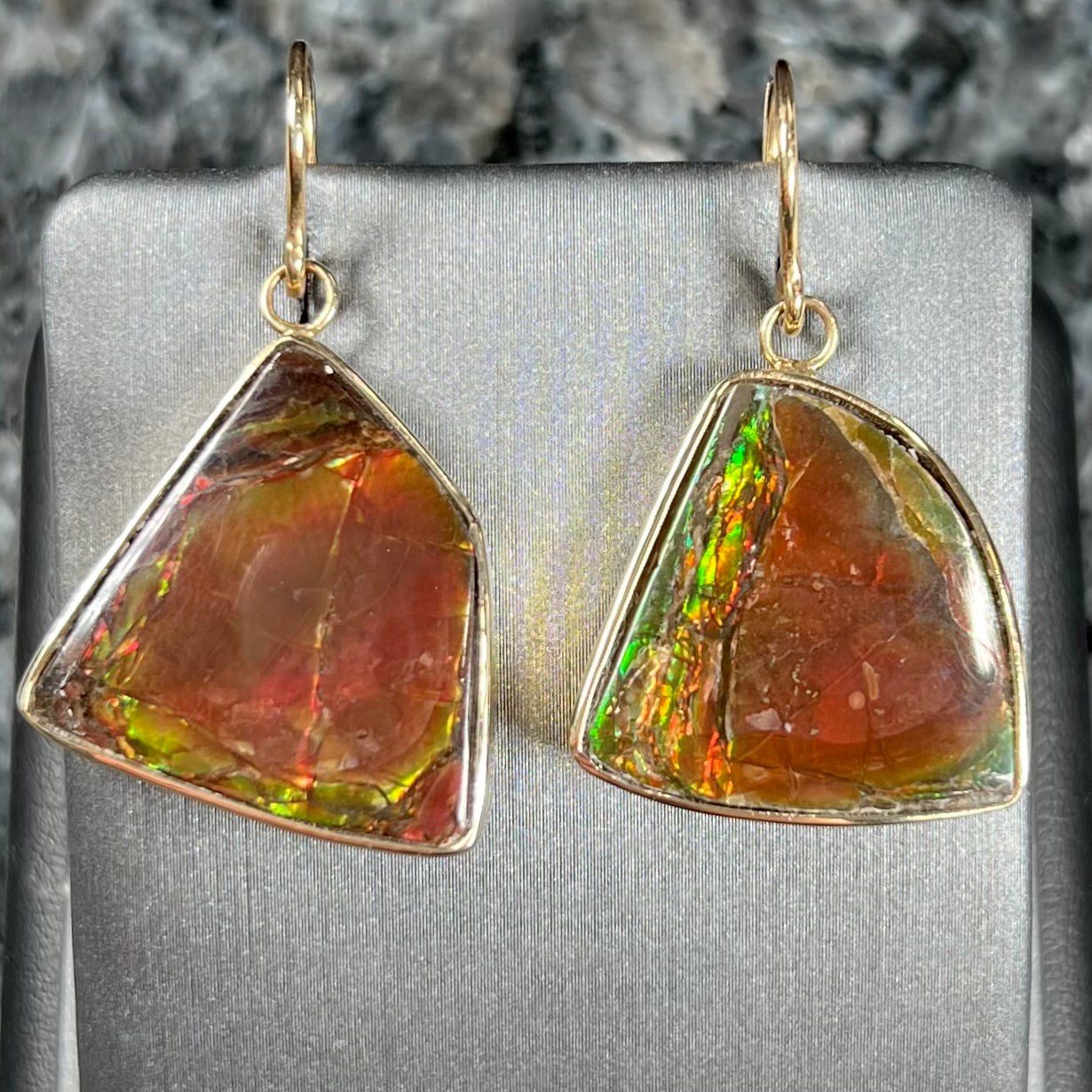 Yellow gold French wire dangle earrings bezel set with two polished freeform cut red ammolite fossils.