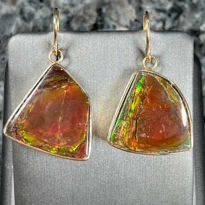 Yellow gold French wire dangle earrings bezel set with two polished freeform cut red ammolite fossils.