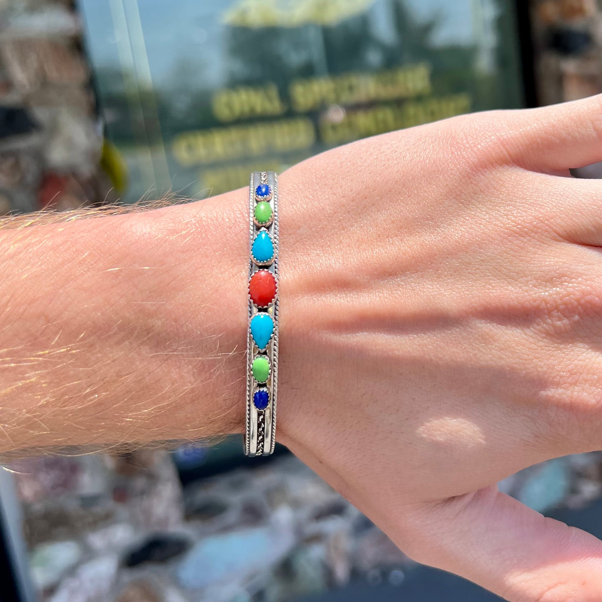 A silver rope cuff bracelet set with coral, turquoise, gaspeite, and lapis lazuli stones.  The underside is stamped "Daniel Mike".