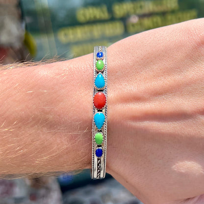A silver rope cuff bracelet set with coral, turquoise, gaspeite, and lapis lazuli stones.  The underside is stamped "Daniel Mike".
