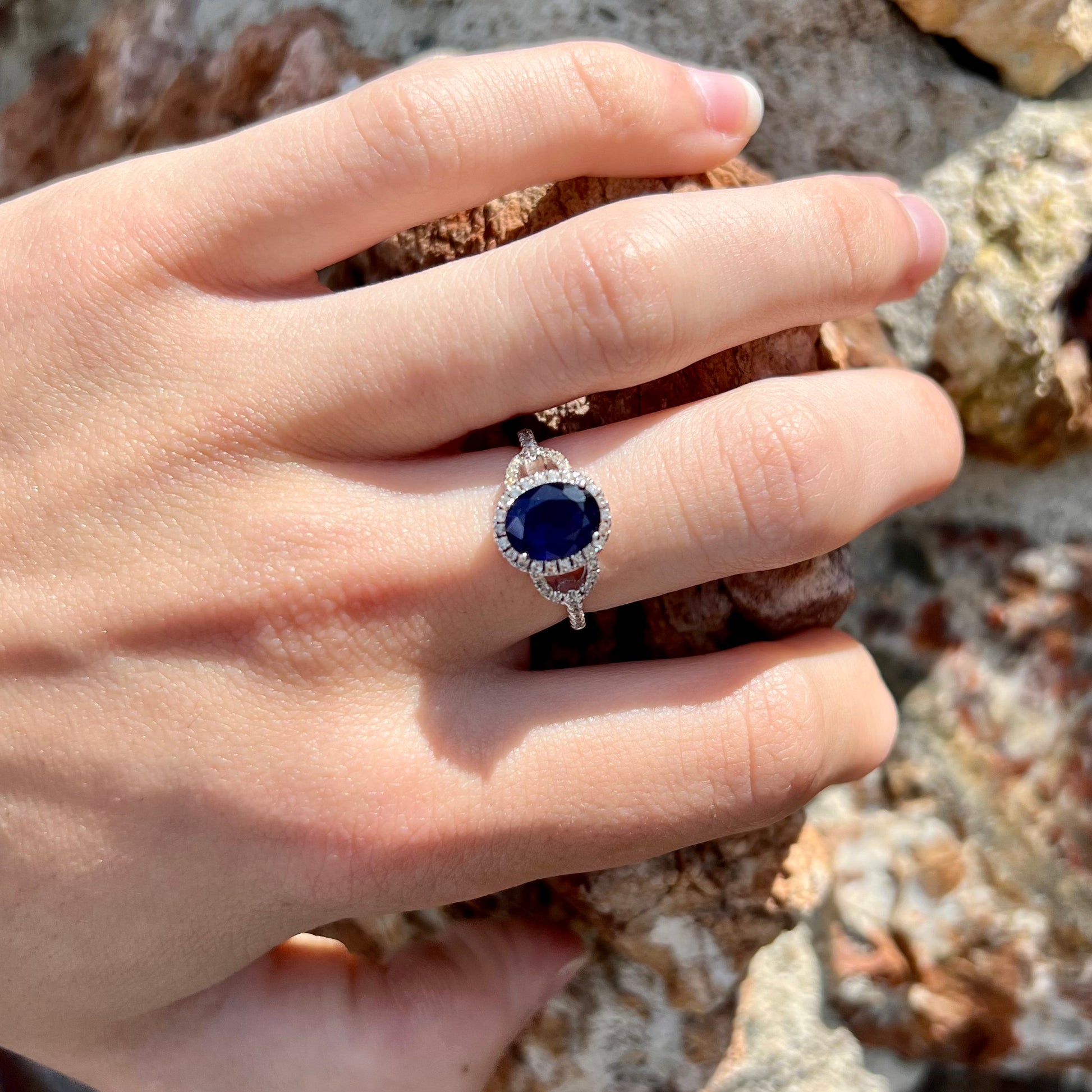A sterling silver, white zircon halo ring set with an oval cut blue sapphire.