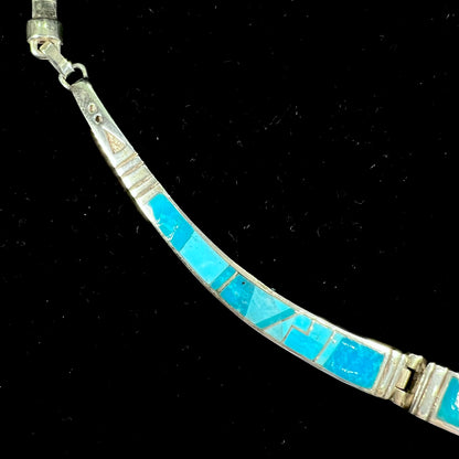 A silver omega style necklace inlaid with turquoise under the watch of David Rosales.
