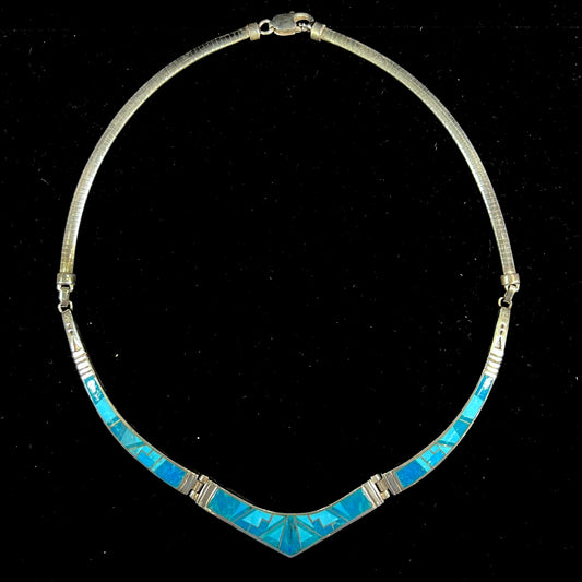 A silver omega style necklace inlaid with turquoise under the watch of David Rosales.