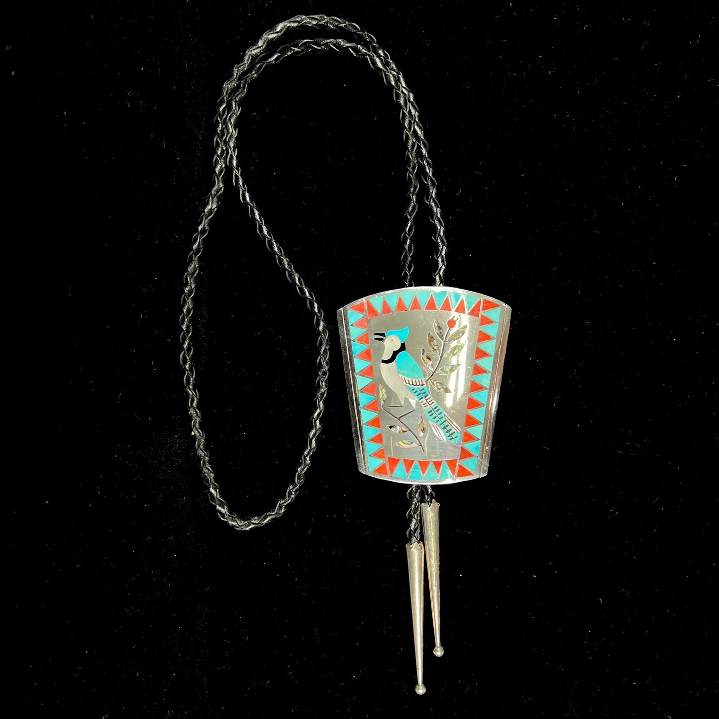 A turquoise and coral inlay bolo tie featuring the motif of a blue jay bird, handmade by Zuni artists Dennis and Nancy Edaakie.