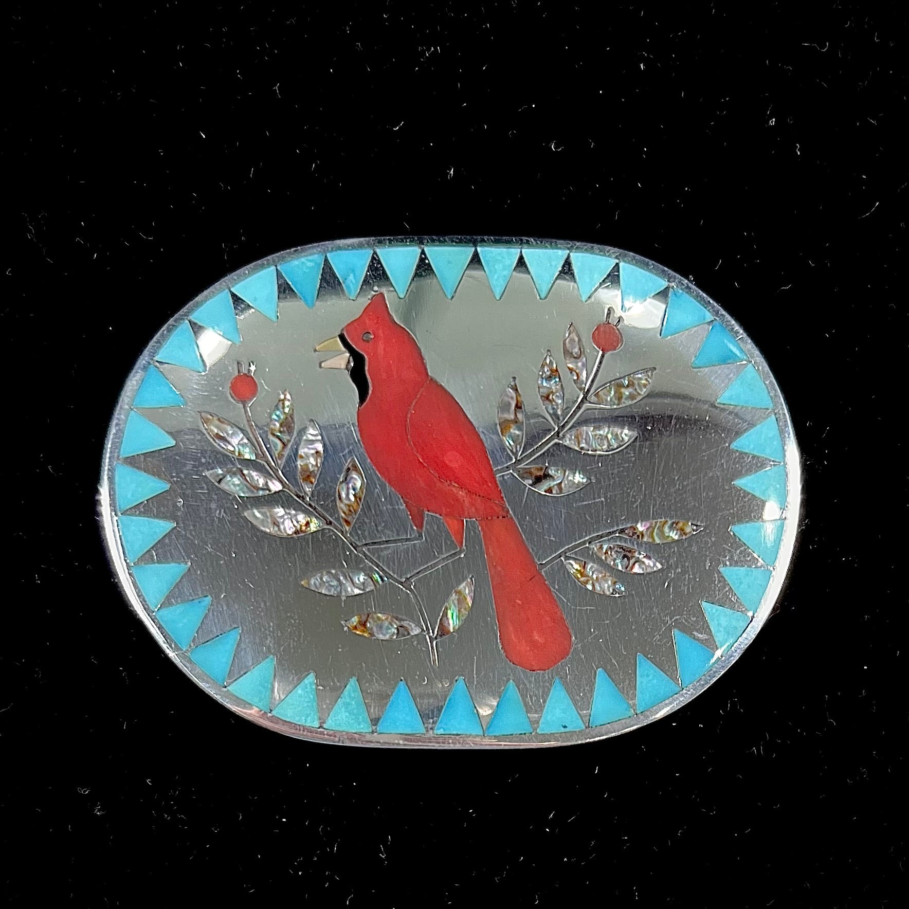 A Zuni belt buckle featuring a red cardinal inlaid with coral, handmade by artists Dennis and Nancy Edaakie.