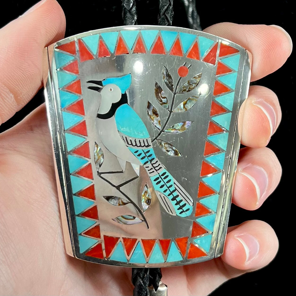 A turquoise and coral inlay bolo tie featuring the motif of a blue jay bird, handmade by Zuni artists Dennis and Nancy Edaakie.