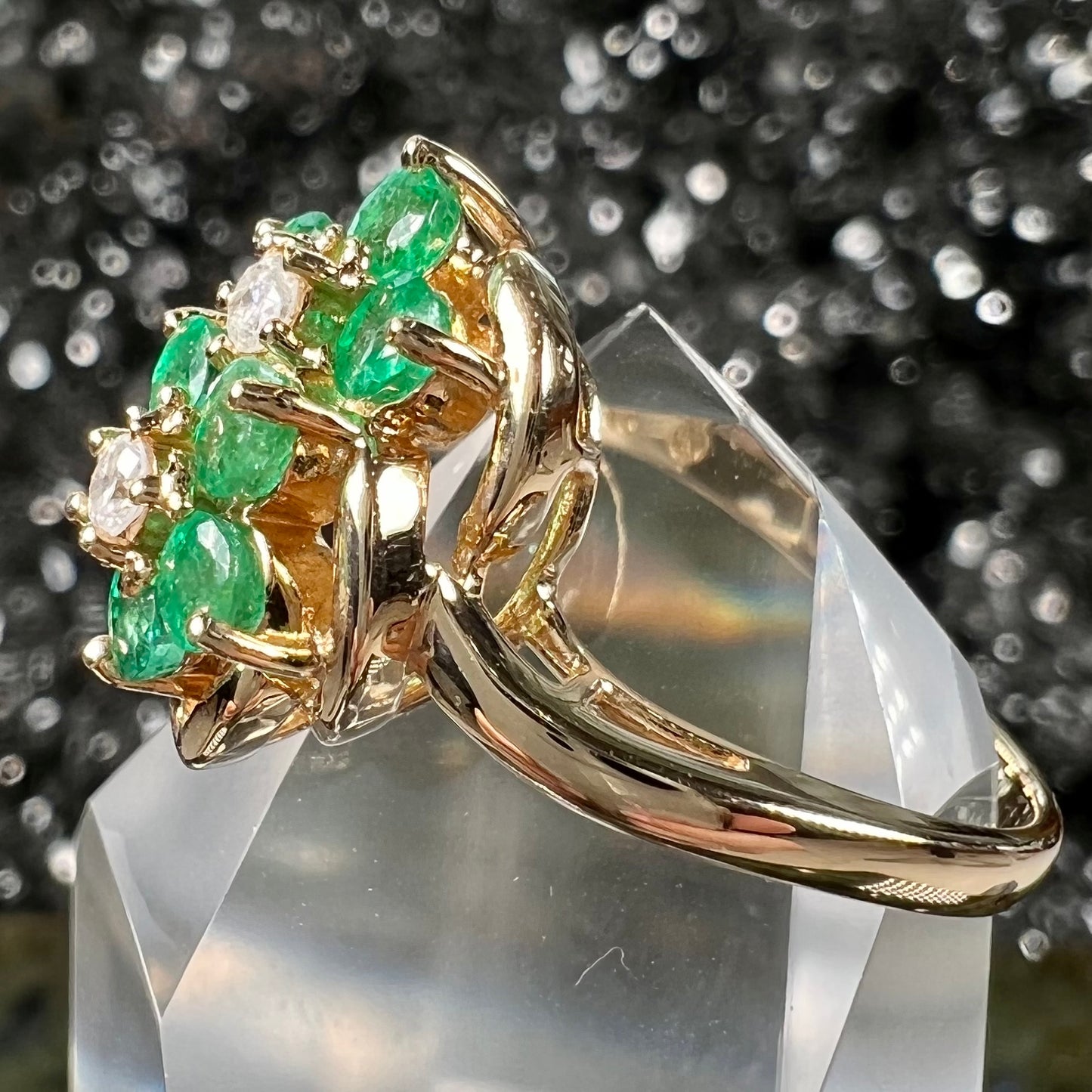 A yellow gold ring set with round cut emerald and diamonds that form the shape of two flowers.