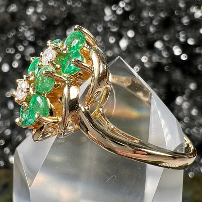 A yellow gold ring set with round cut emerald and diamonds that form the shape of two flowers.