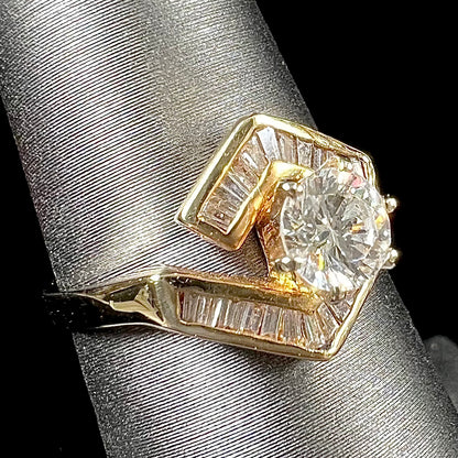 A gold diamond ring set with a round cut center stone with channel set baguette cut accent stones.