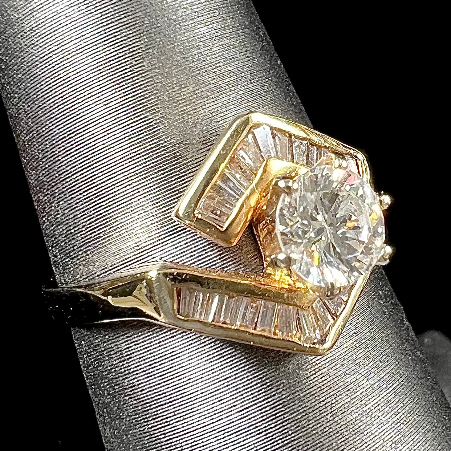 A gold diamond ring set with a round cut center stone with channel set baguette cut accent stones.