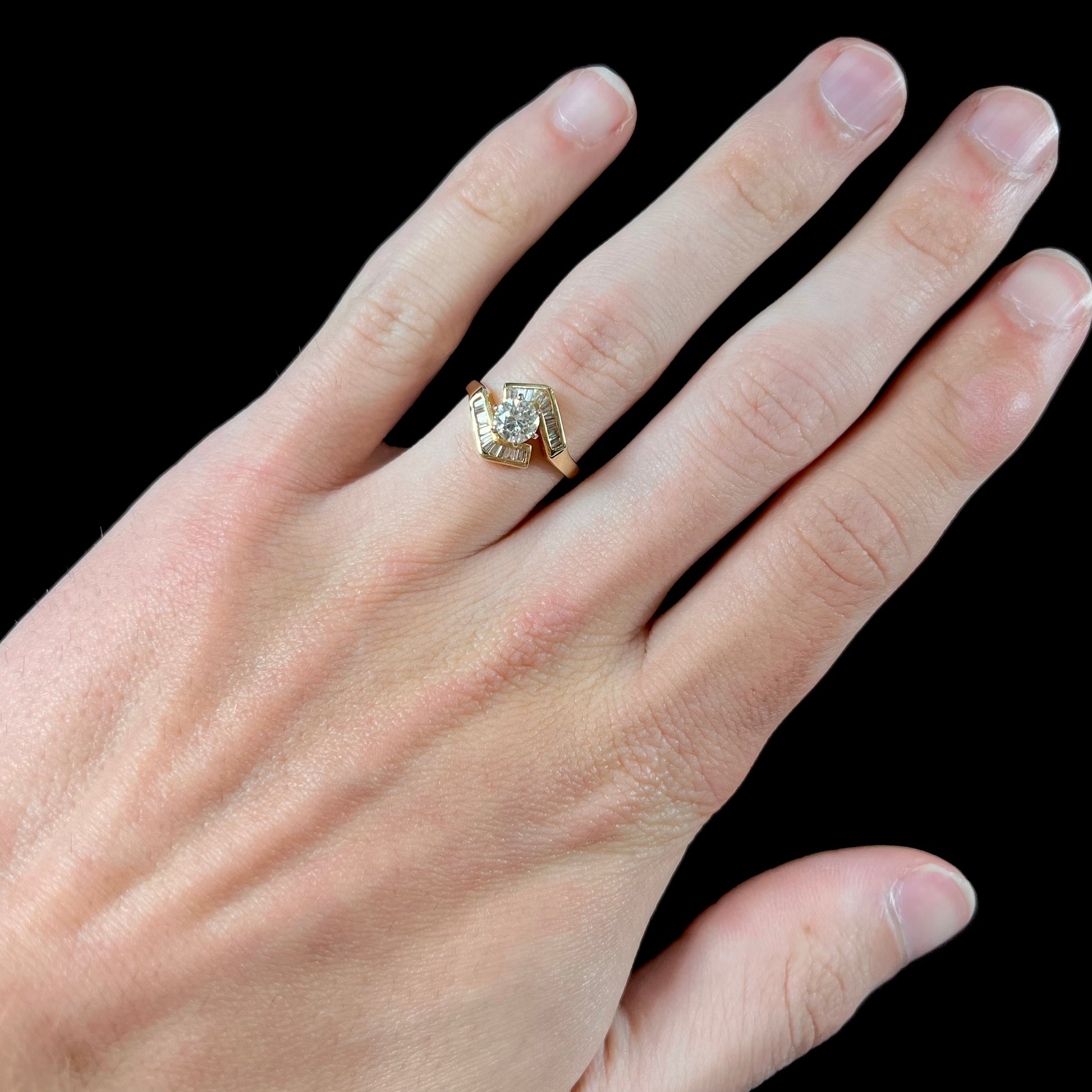 A gold diamond ring set with a round cut center stone with channel set baguette cut accent stones.