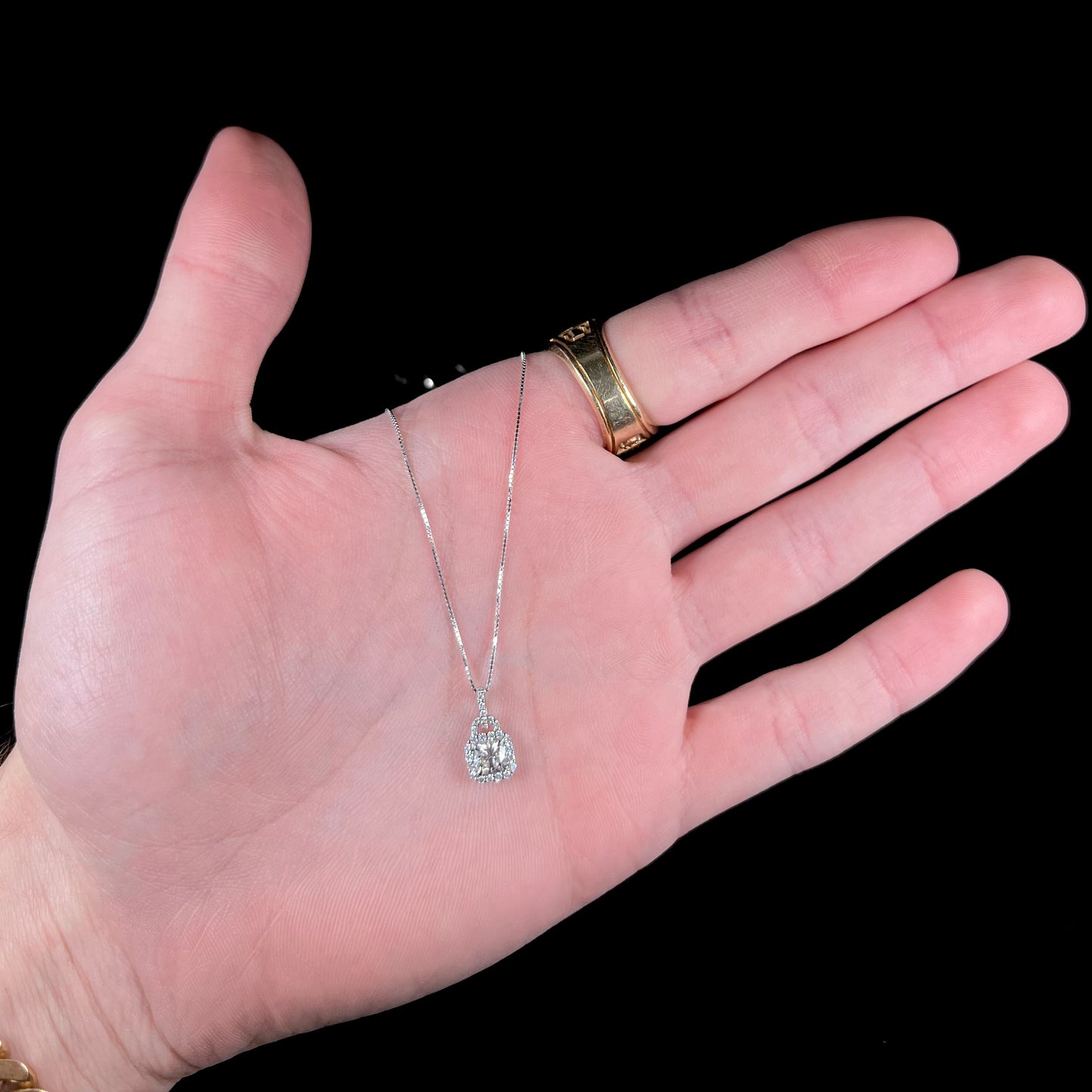 A ladies' platinum diamond halo necklace set with a 0.58ct cushion cut diamond on a box chain.