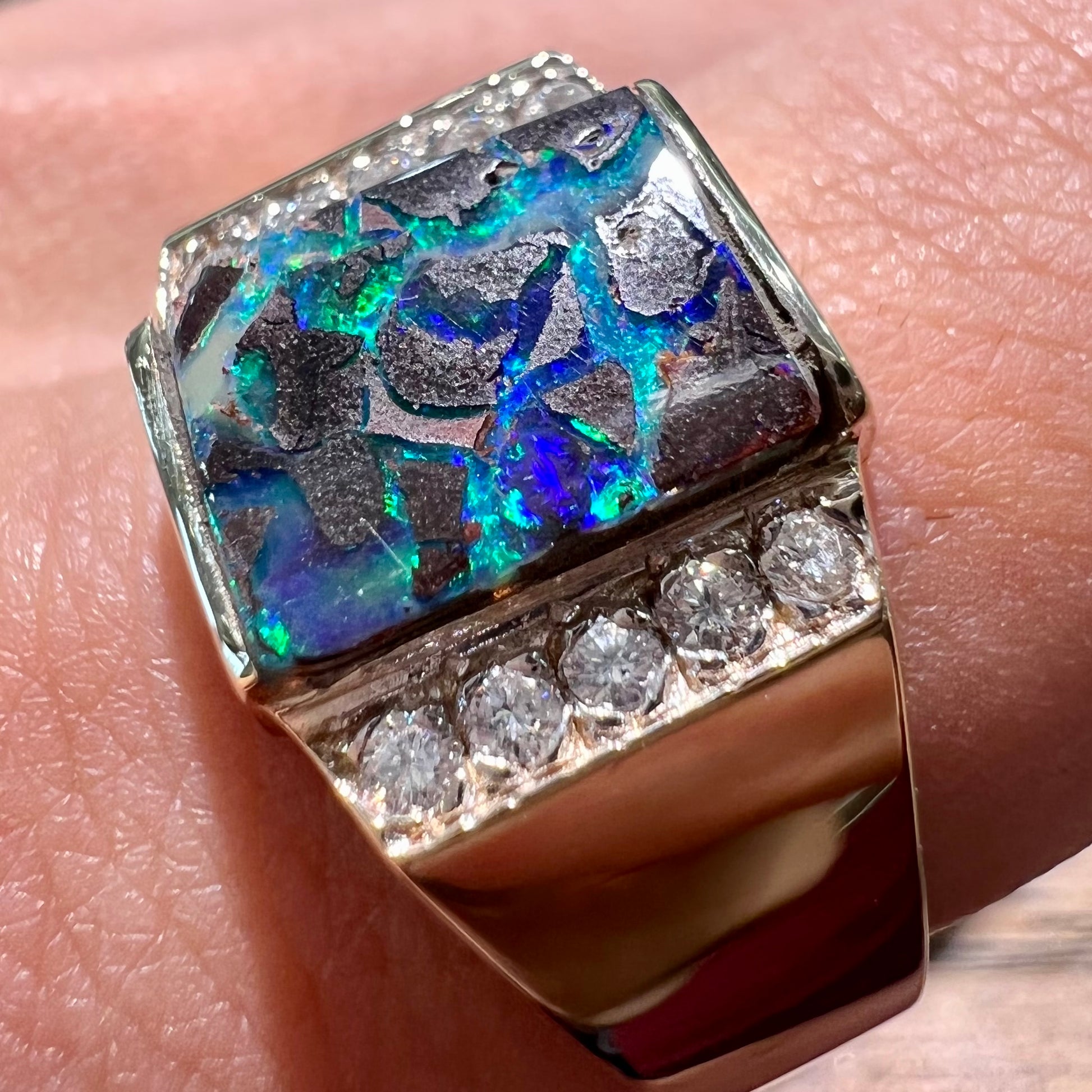 A men's gold boulder opal and diamond ring.  The opal shows blue and green colors.