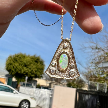 A triangular gold pendant set with five round diamonds and a white crystal opal with green fire.