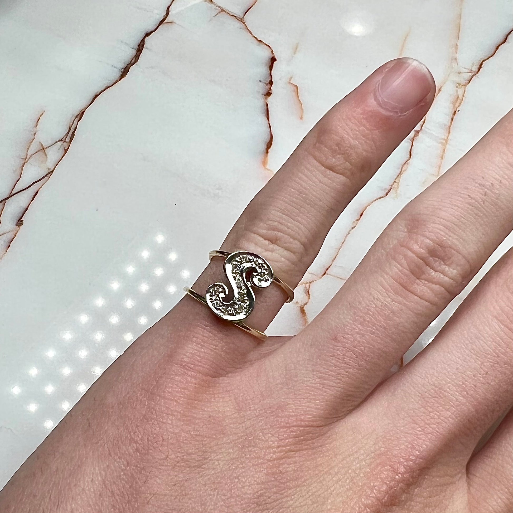 A two tone white and yellow gold initial ring of the letter "S" set with diamonds.
