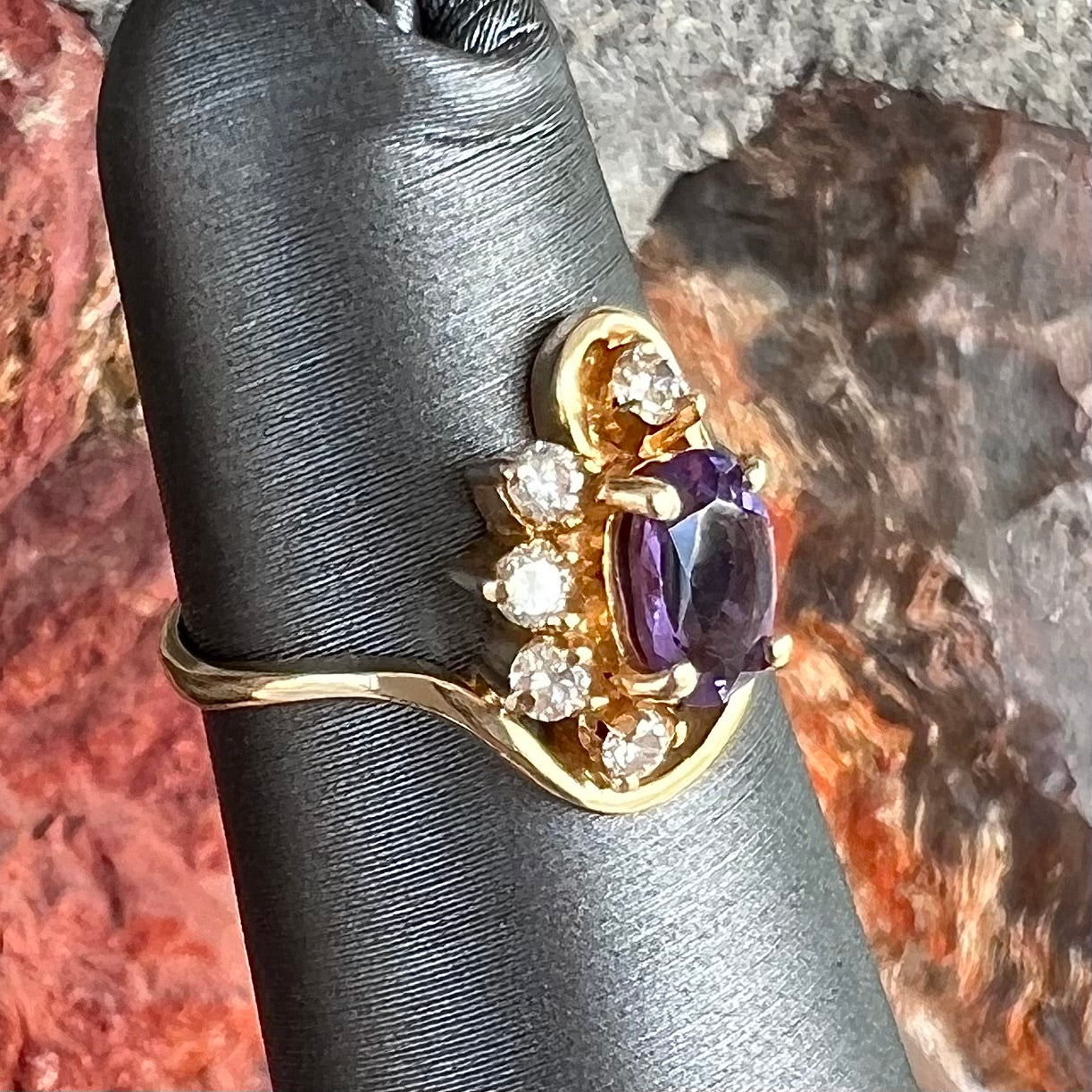 A ring made with 14 karat yellow gold, diamonds, and an amethyst.  The ring has a swoosh style.