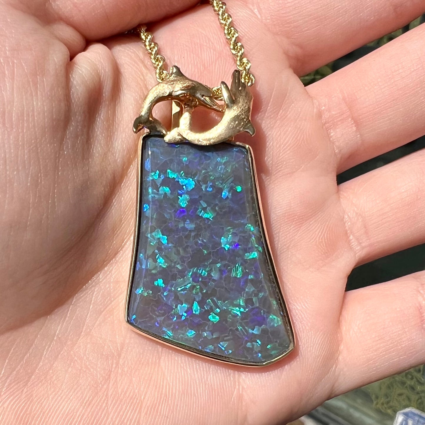 A gold freeform cut black opal bezel pendant cast with two dolphins on top of the opal.