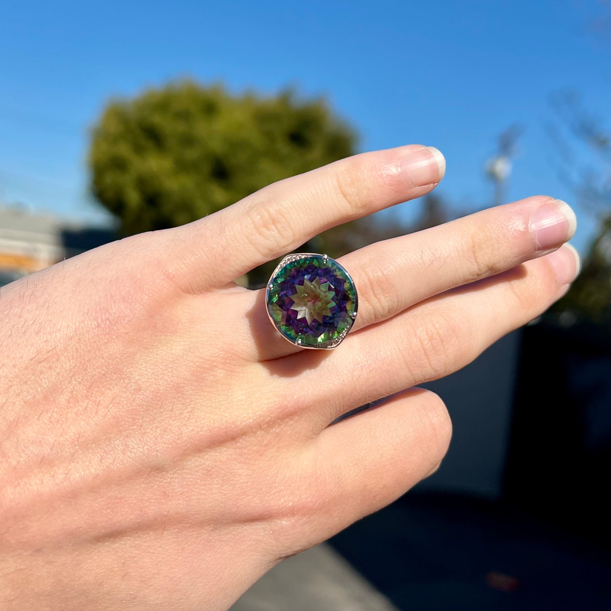 A large, round cut pink and green mystic topaz set in a sterling silver ring with white topaz accent stones.