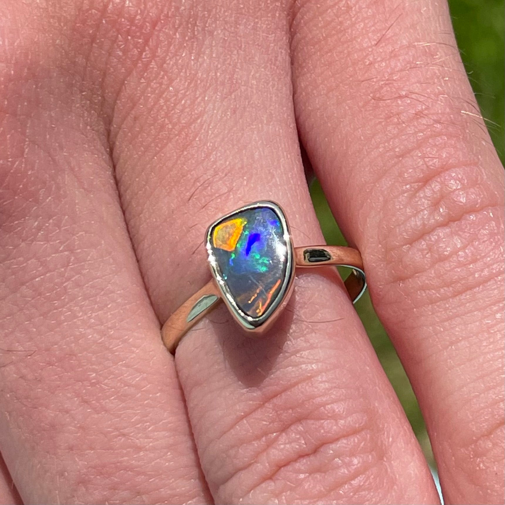 A handmade yellow gold solitaire ring bezel set with a Lightning Ridge red-on-black harlequin opal.