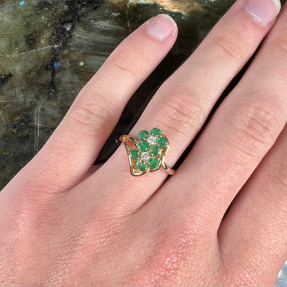 A yellow gold ring set with round cut emerald and diamonds that form the shape of two flowers.